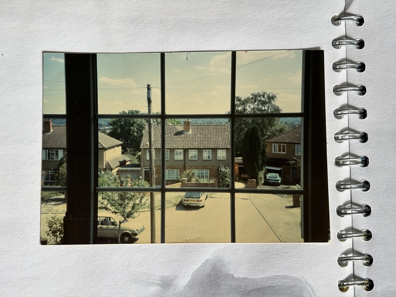 Photograph of a cul-de-sac through a window, telegraph pole, wires, cars, trees, houses and clouds